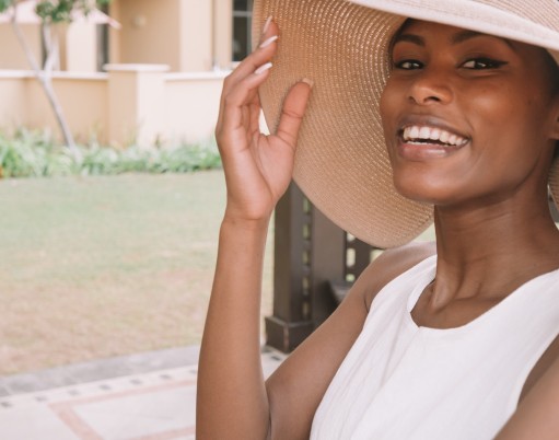 woman pushing up big hat and smiling outside