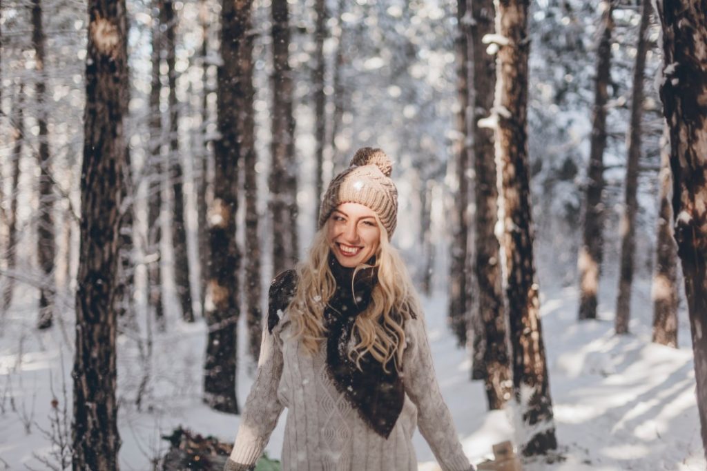 woman in sweater and beanie smiling in a snowy forest