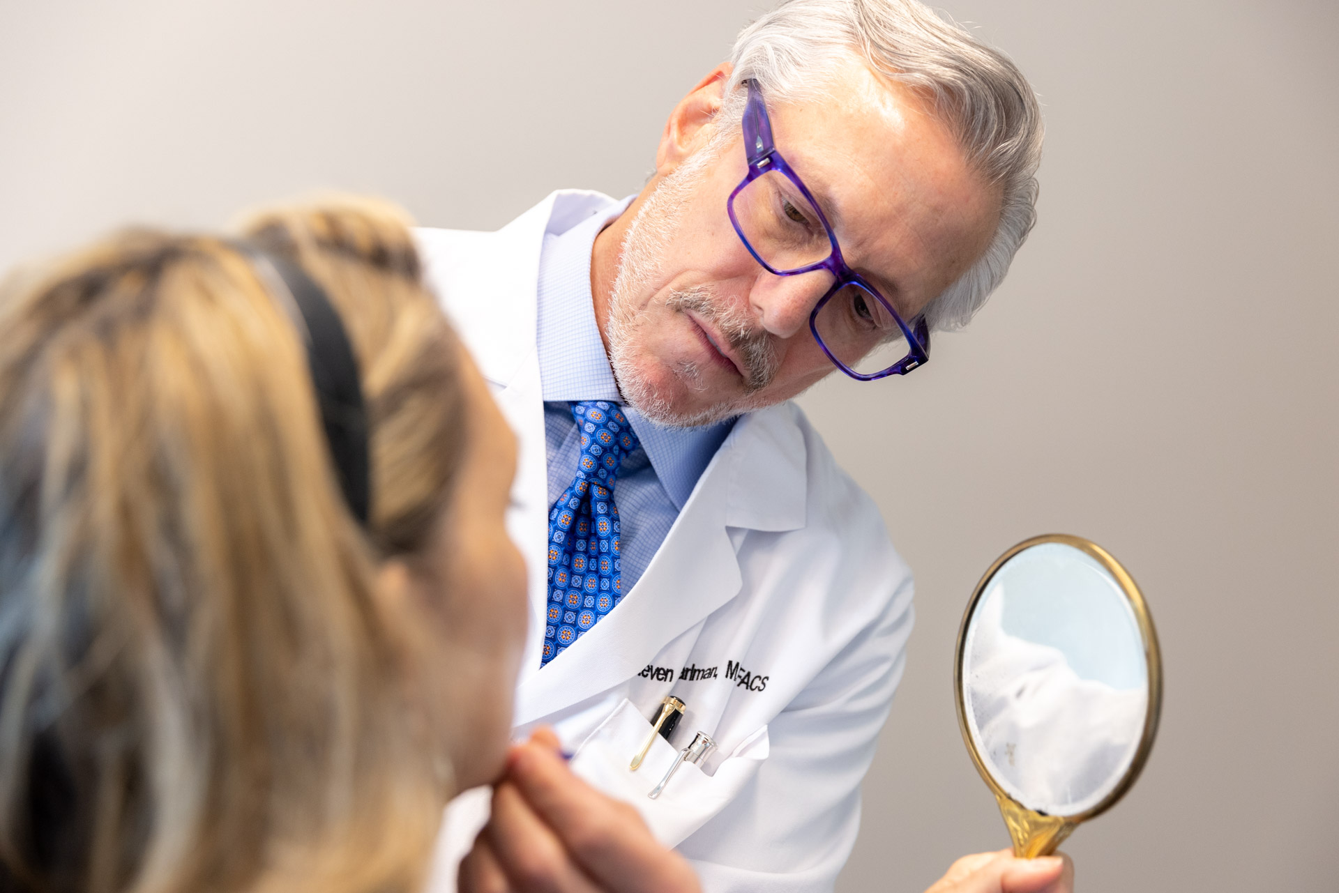 Dr. Pearlman looking at woman's chin with mirror