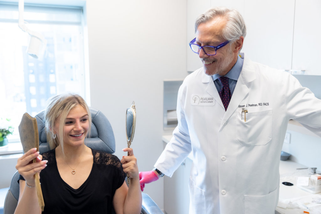 female patient with mirrors admiring her surgical results after paying the Otoplasty Cost in NYC