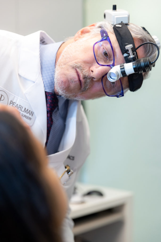Dr. Pearlman, considered one of the best rhinoplasty surgeons in NYC, looking at patient's nose with headset during rhinoplasty consultation