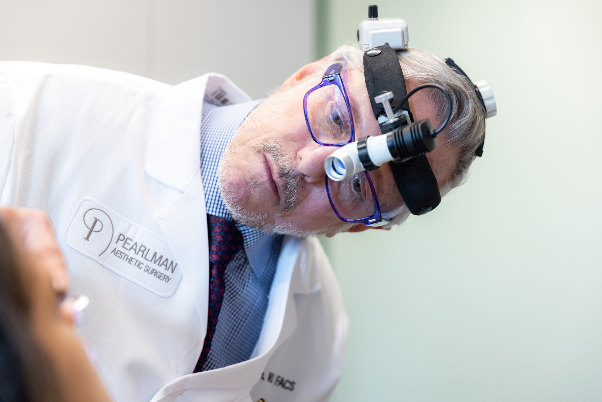 Dr. Pearlman looking at patient's nose with headset during rhinoplasty consultation