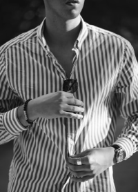 adjusting striped button up shirt with sunglasses in hand
