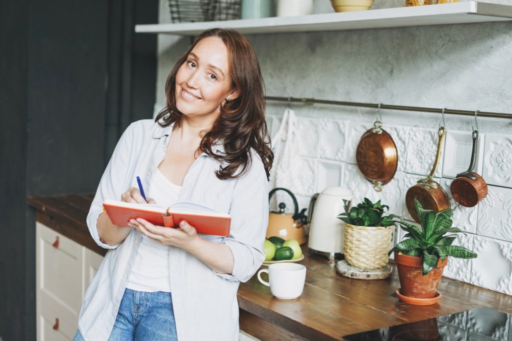 woman smiling and writing in a book in her kitchen