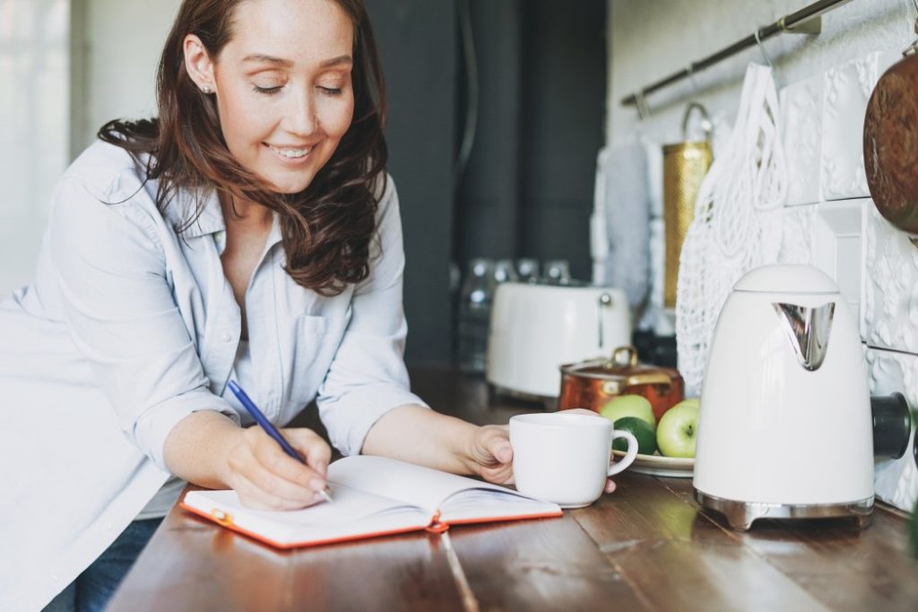 woman smiling with coffee and writing in journal