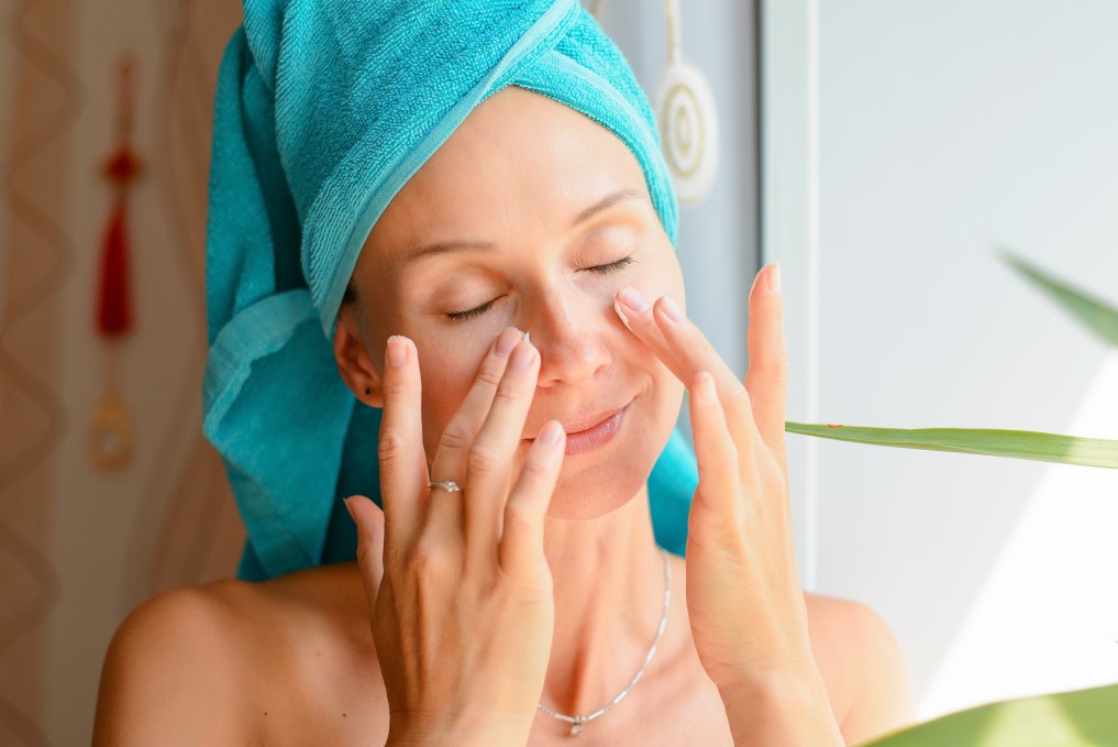 woman with blue hair towel putting lotion on face