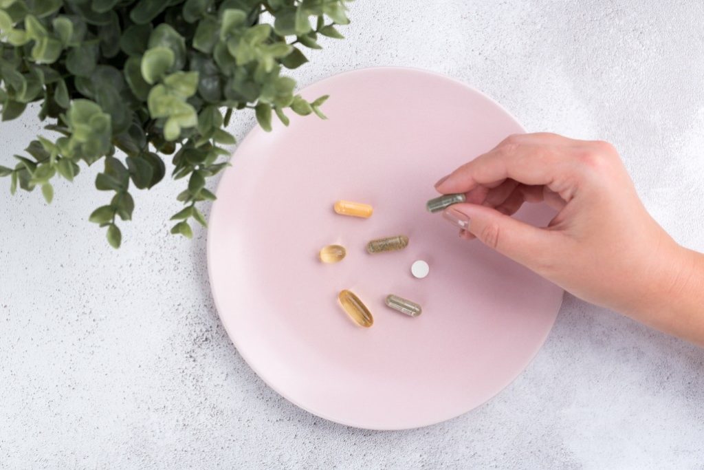 woman putting vitamins on a pink plate by plant