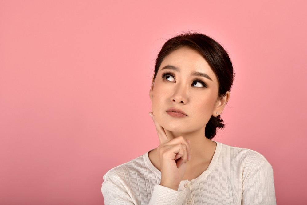 woman thinking with hand on face in front of pink wall