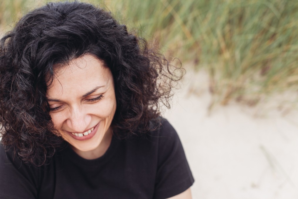 curly haired woman smiling at the beach