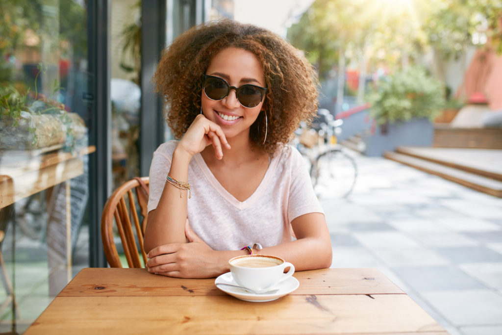 woman with coffee smiling with sunglasses on outside