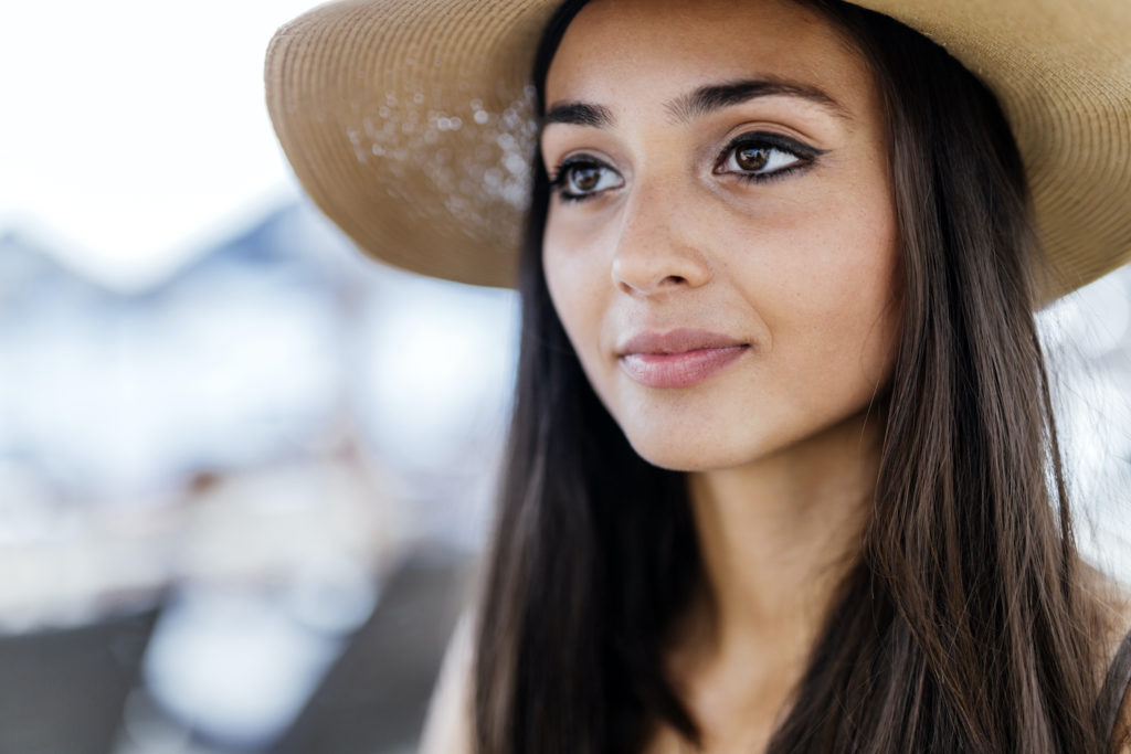 brunette woman smiling with eyeliner and hat