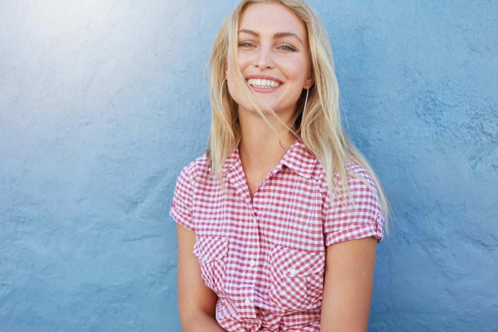 blonde woman in plaid top smiling in front of blue wall
