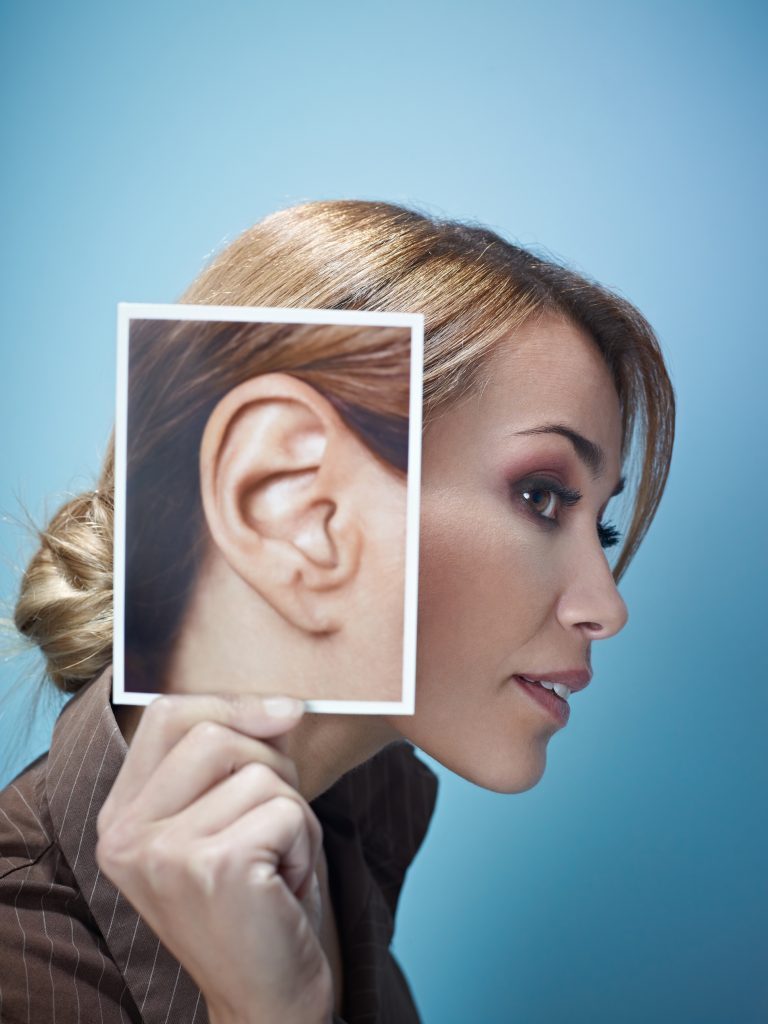 woman holding top image of large ear to her ear