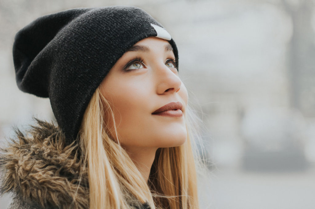 blonde woman in beanie and furry coat looking up