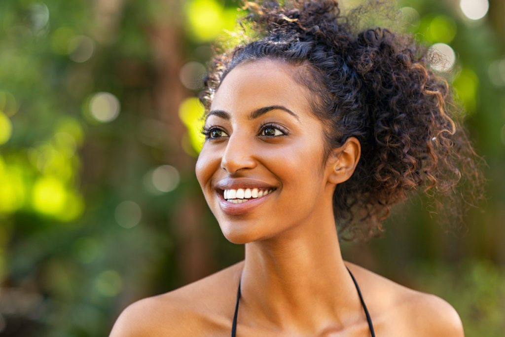 woman with curly hair in ponytail smiling outside