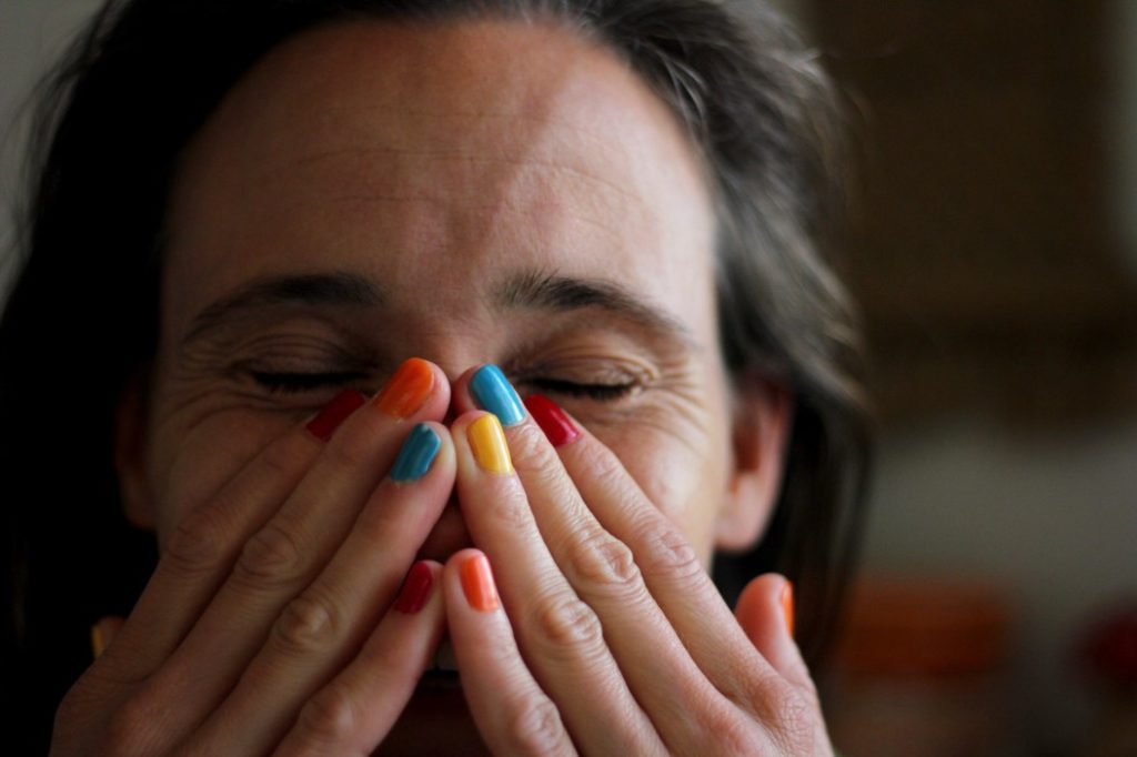 woman with different colored nails covering face with eyes closed