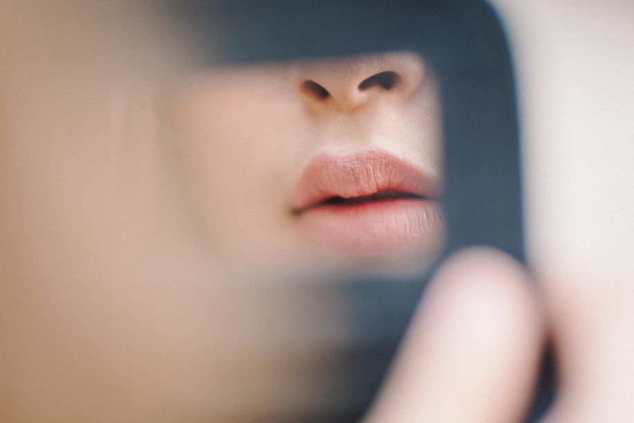 woman holding up mirror in front of lips