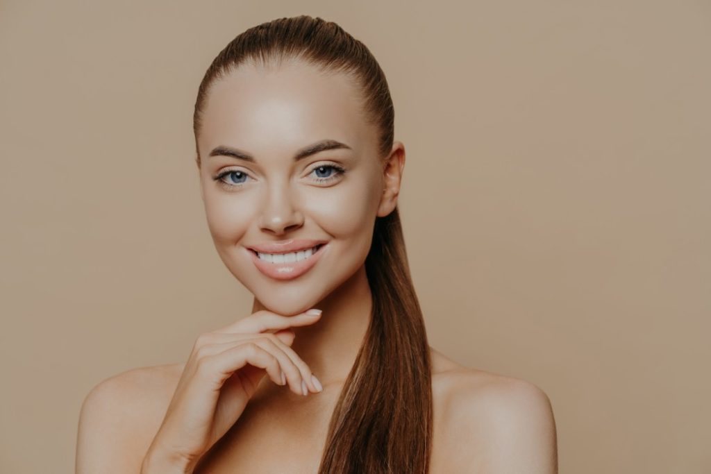 woman with ponytail smiling with hand on chin