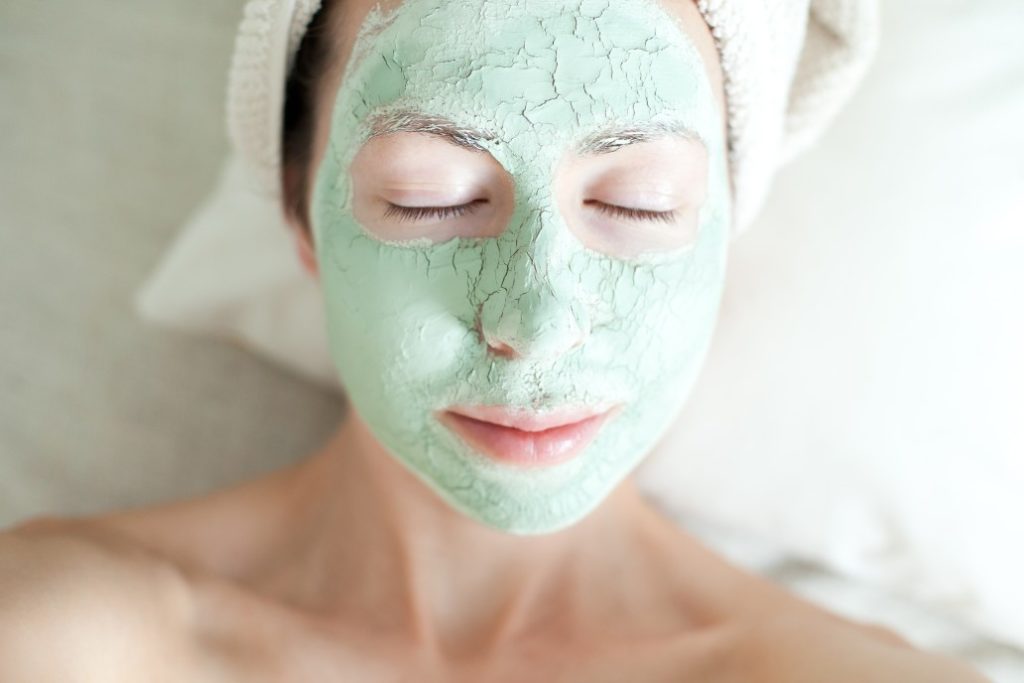cracking green face mask on woman with hair towel