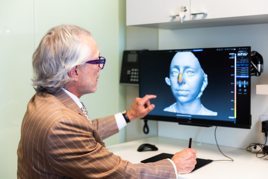 Photo of Dr. Pearlman seated in front of a computer screen reviewing 3D image of a nose.